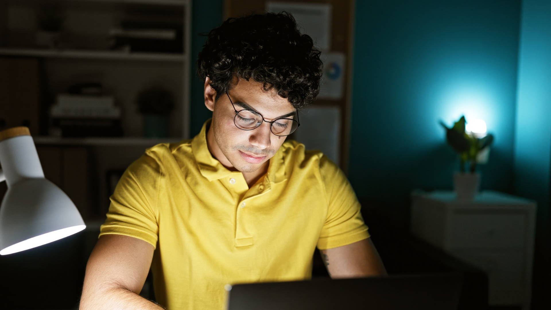 A young man working late at a laptop in a dim office