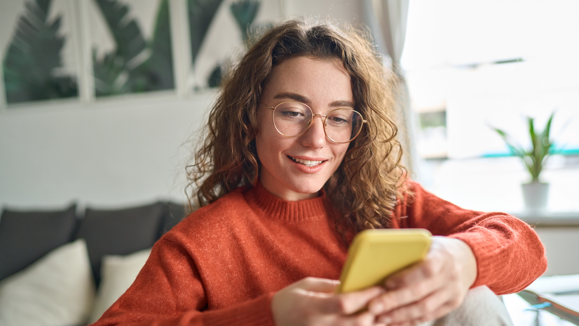 A young woman smiling while using her phone at home