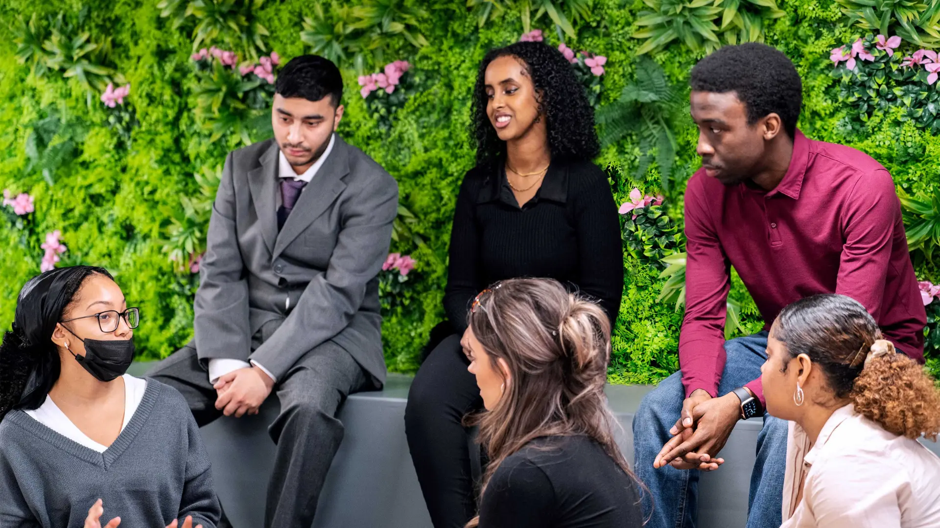 A group of young professionals talking together in front of a green plant wall