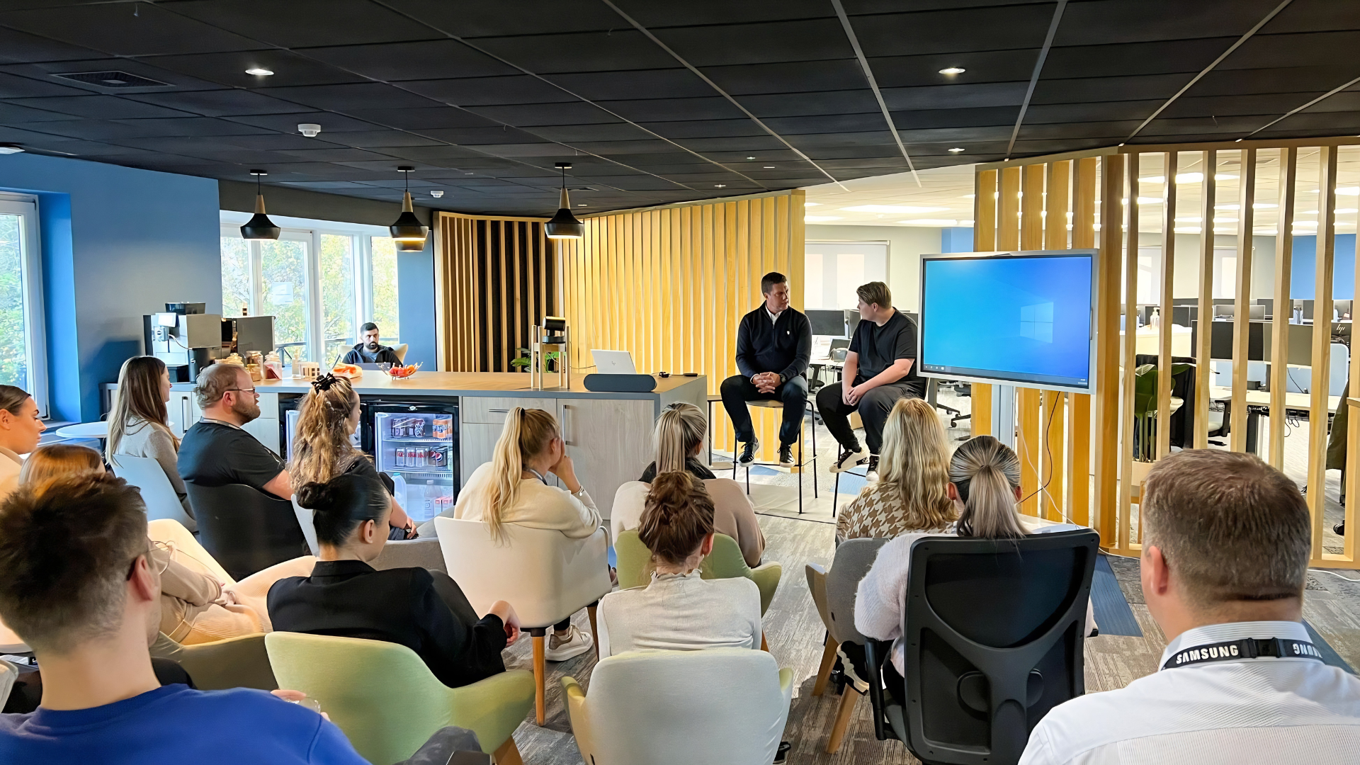 A team listening to a fireside conversation in an open plan office